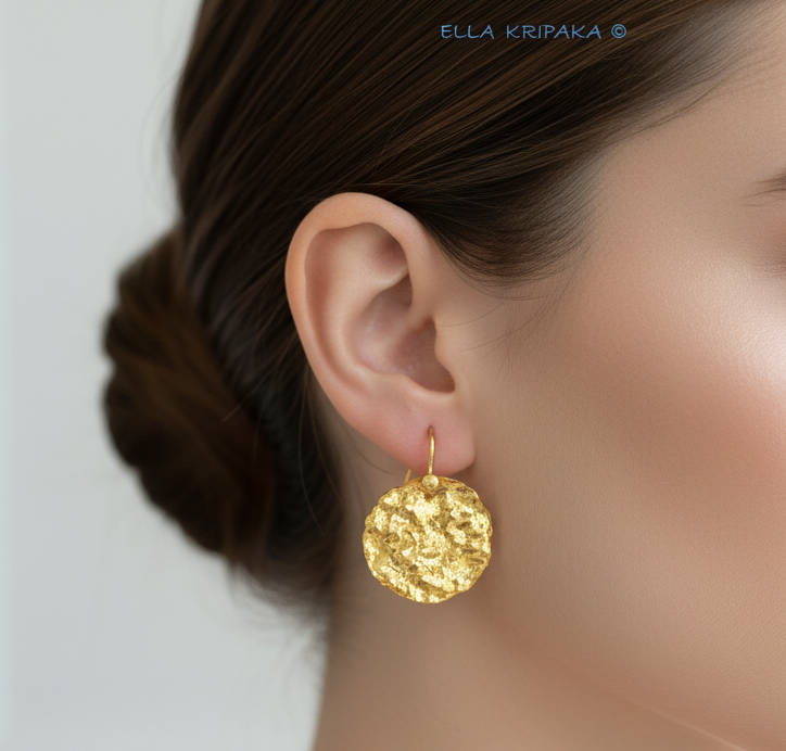 Organic 24k 9999 gold hammered wavy disk earrings with shiny gold textures worn by a woman and on grey background, artist-jeweler's name 'Ella Kripaka'