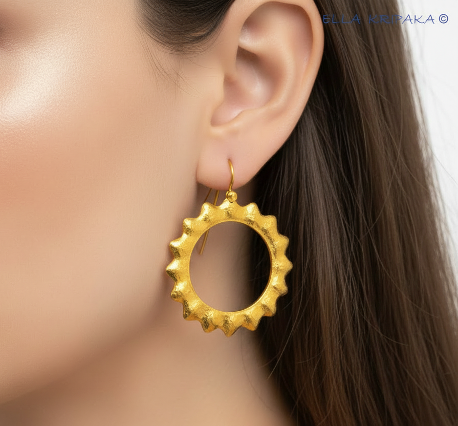 Solid 24k gold hammered Hoops Sun earrings with hook clasp and shiny forged gold textures worn by a woman,  name 'ELLA KRIPAKA' written with tiny blue letters upper right