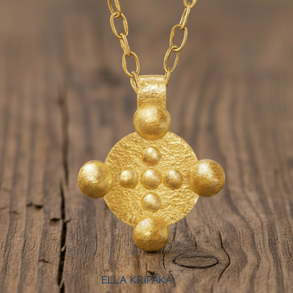 24k 9999 gold hammered Byzantine disk pendant with forged gold textures is on a old woiden surface, artist's name 'Ella Kripaka'