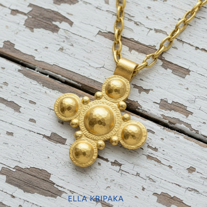24k 9999 gold hammered Byzantine cross pendant with shiny forged gold textures is on a old white wooden surface, artist's name 'Ella Kripaka'