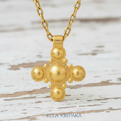 24k 9999 gold hammered Byzantine cross pendant with shiny forged gold textures is on a old white wooden surface, artist's name 'Ella Kripaka'