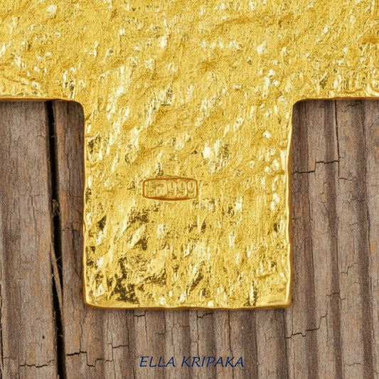 Hallmark 999 on 24k gold cross pendant with hammered textures on rustic wooden surface, with 'Ella Kripaka' branding