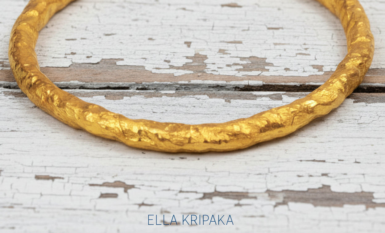 Organic hammered 24k 9999 gold bracelet uneven bangle on a old white wooden background, branding artist-jeweler name 'Ella Kripaka'