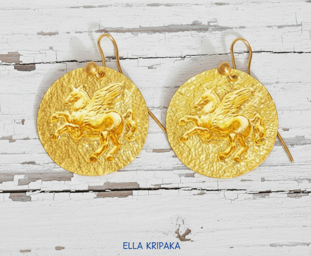 Hammered 24k Gold 9999 gold disk earrings with convex Pegasus and with forged textured gold on old white wooden background, branded artist's name 'Ella Kripaka' 