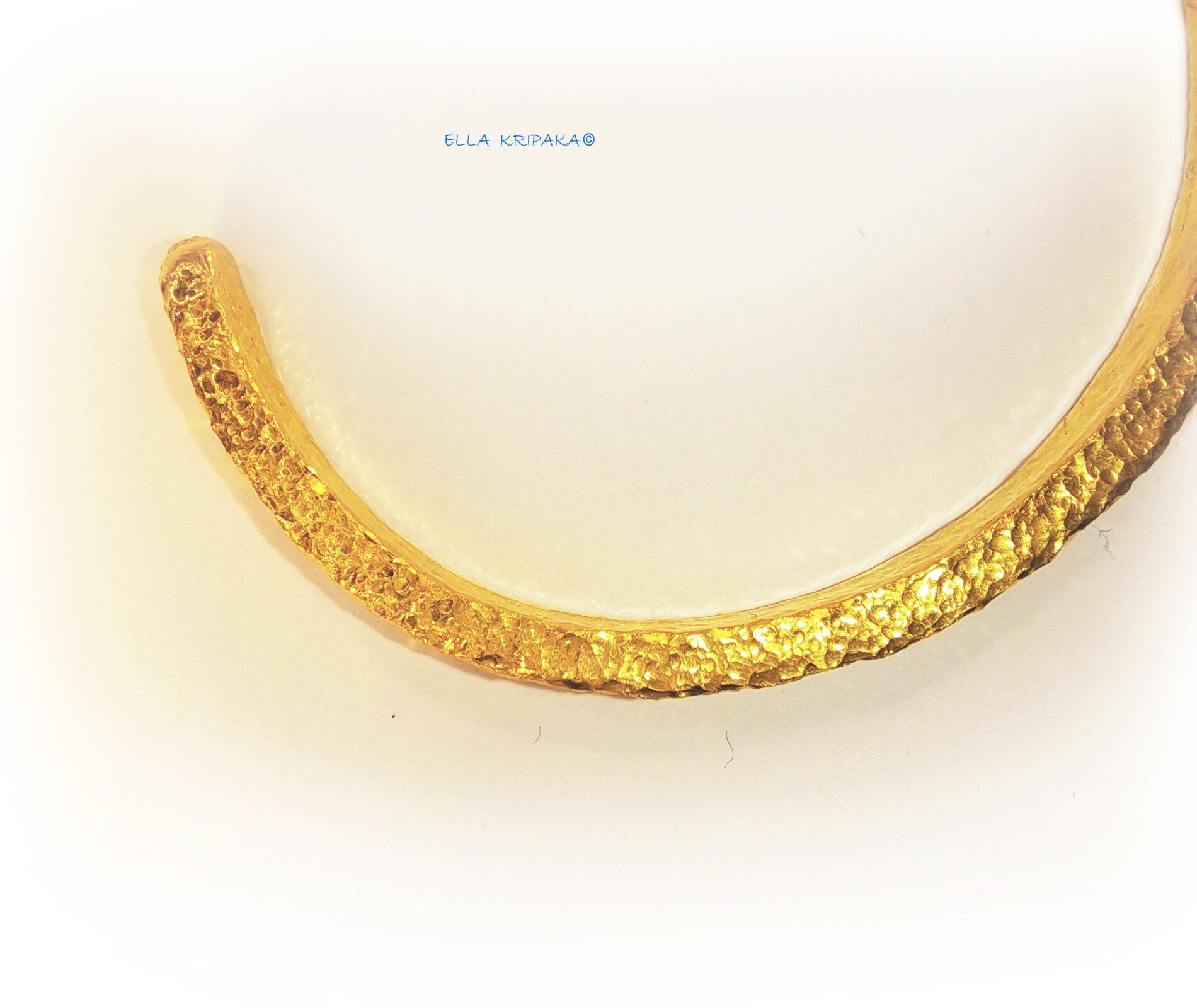 Hammered 24k 9999 gold cuff thick bracelet Ancient Rome style on a white background, artist-jeweler name 'Ella Kripaka' branding