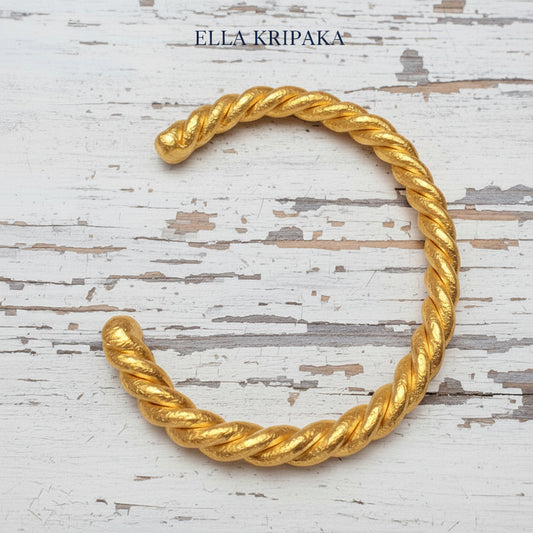 Twisted Viking Hammered 24k 9999 gold bracelet thick cuff on a old white wooden background, branding artist-jeweler name 'Ella Kripaka'