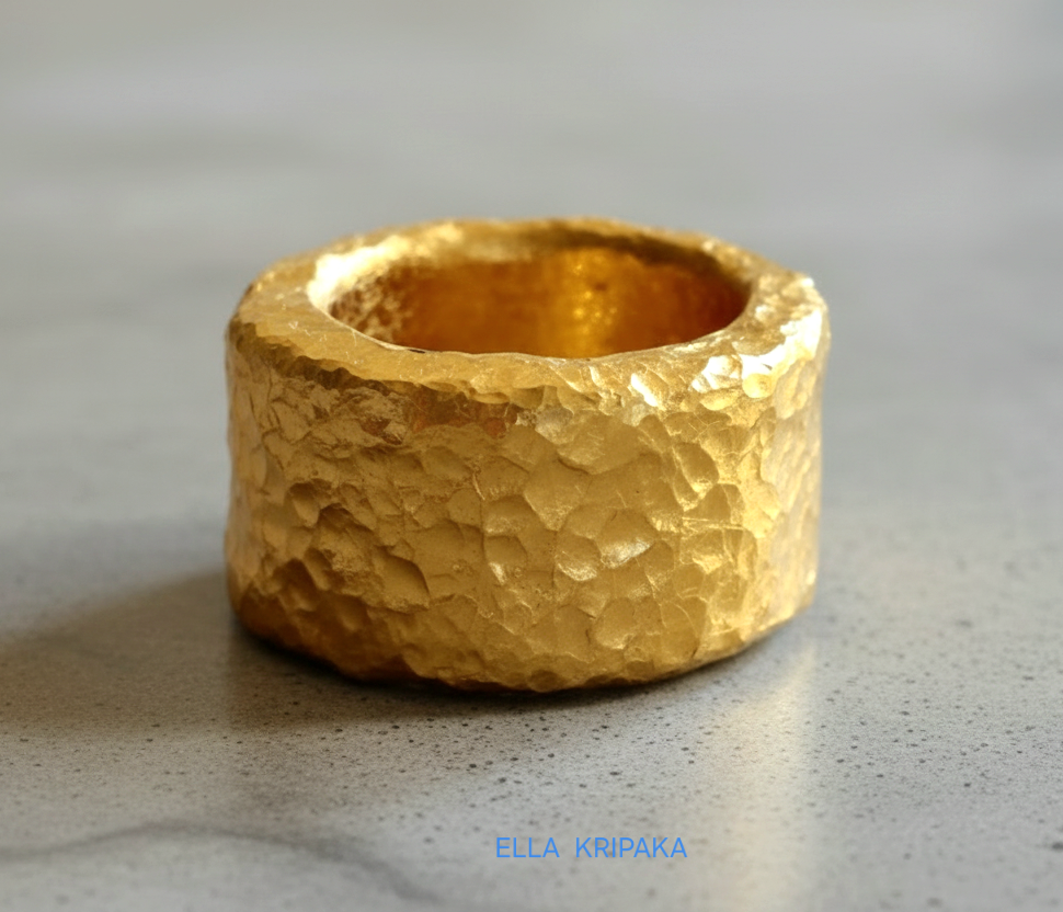 Hammered 24k 9999 Gold thick ring Ancient Rome style with textured gold on a grey concrete background, branded 'Ella Kripaka'