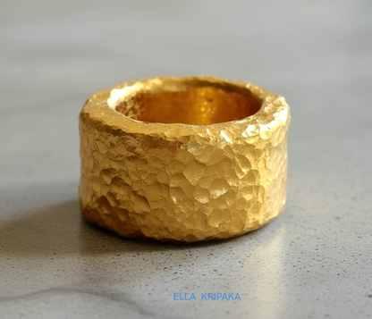 Hammered 24k 9999 Gold thick ring Ancient Rome style with textured gold on a grey concrete background, branded 'Ella Kripaka'