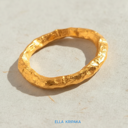 Organic 24k gold hammered ring with uneven textured surface on a light beige craft paper background, branded 'Ella Kripaka'
