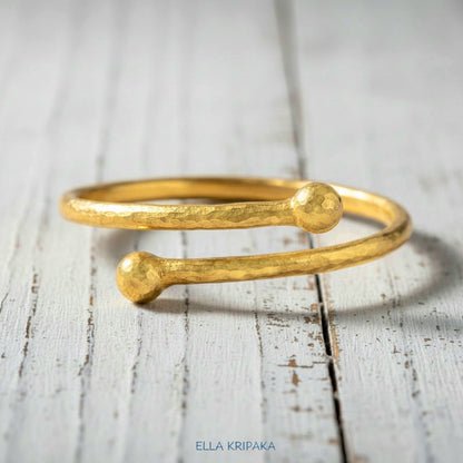 Twisted 24k gold hammered bracelet with thick convex rounds ends and with textured design on white rustic wooden surface, branded artist-jeweler 'Ella Kripaka'