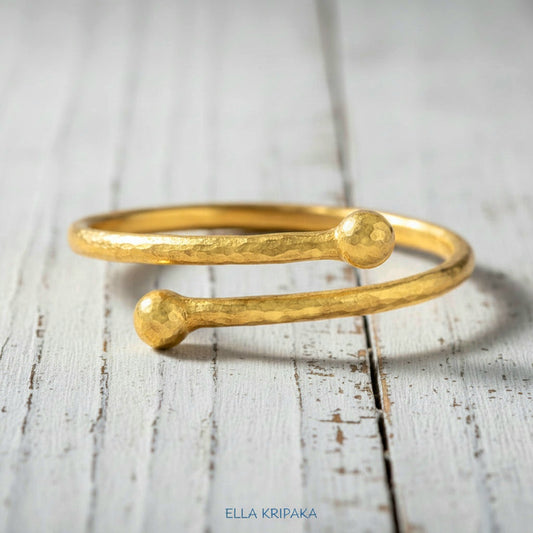 Twisted 24k gold hammered bracelet with thick convex rounds ends and with textured design on white rustic wooden surface, branded artist-jeweler 'Ella Kripaka'