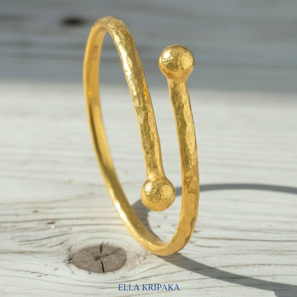 Twisted 24k gold hammered bracelet with thick convex rounds ends and with textured design on light rustic wooden surface, branded artist-jeweler 'Ella Kripaka'