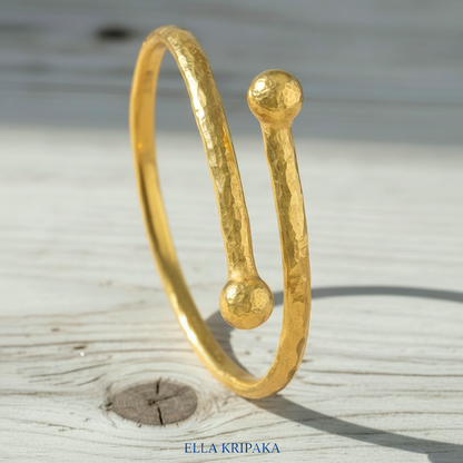 Twisted 24k gold hammered bracelet with thick convex rounds ends and with textured design on light rustic wooden surface, branded artist-jeweler 'Ella Kripaka'