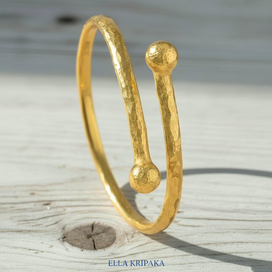 Twisted 24k gold hammered bracelet with thick convex rounds ends and with textured design on light rustic wooden surface, branded artist-jeweler 'Ella Kripaka'