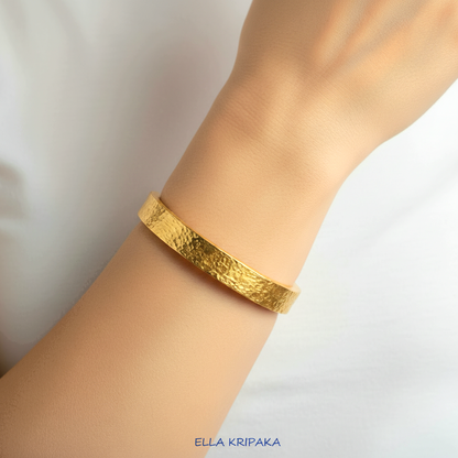 Hammered 24k 9999 Gold thick bangle bracelet Ancient Rome style worn by woman on wrist and on white t-shirt background, artist's name 'Ella Kripaka' branding