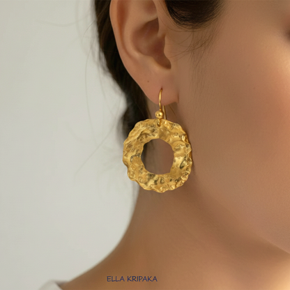 Organic 24k 9999 gold hammered wavy hoops earrings with shiny gold textures worn by a woman and on grey background, artist-jeweler's name 'Ella Kripaka'