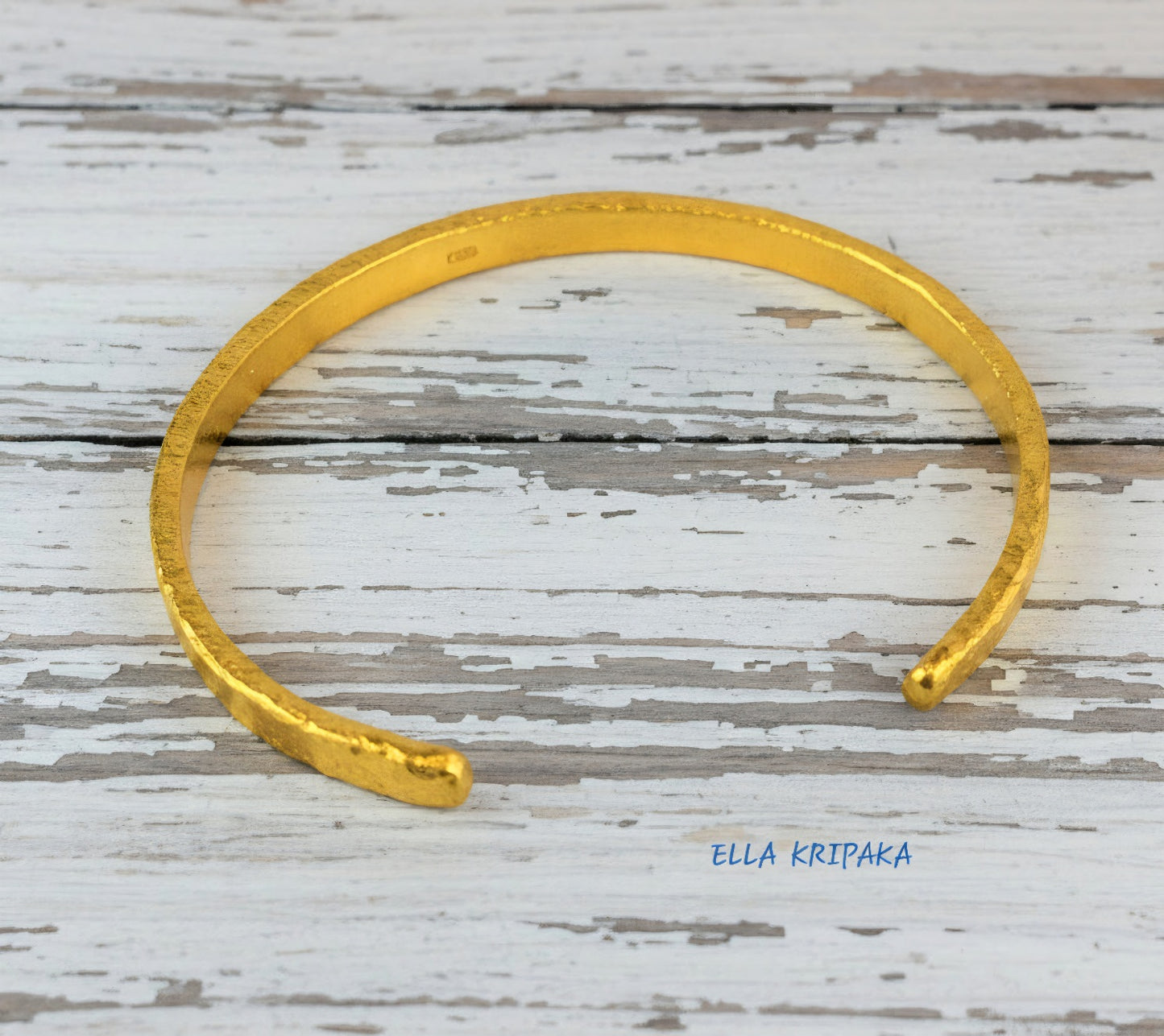 Hammered 24k 9999 gold cuff thick bracelet Ancient Rome style on old white wooden background, artist-jeweler's name 'Ella Kripaka'