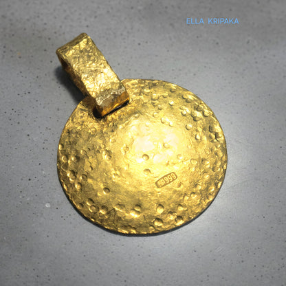 Hammered 24k gold, pure 9999 gold disk pendant with shiny forged gold textures on grey concrete surface, artist-jeweler 'Ella Kripaka' branding