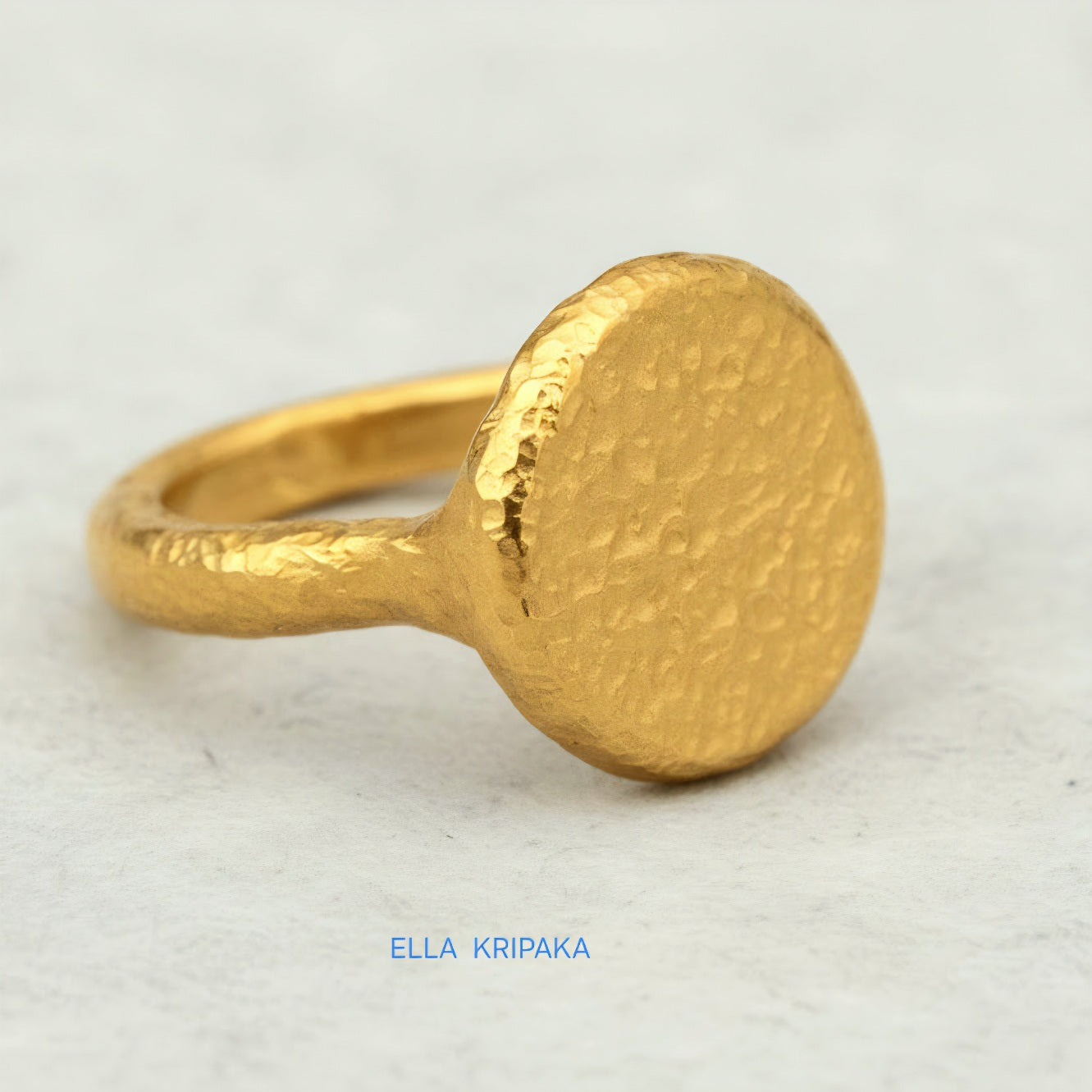 Hammered 24k 9999 Gold thick ring disk signet Ancient Rome style with a textured forged gold surface on a white craft paper background, branded 'Ella Kripaka'