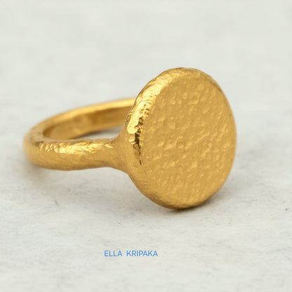 Hammered 24k 9999 Gold thick ring disk signet Ancient Rome style with a textured forged gold surface on a white craft paper background, branded 'Ella Kripaka'