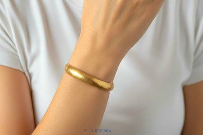 Hammered 24k gold bracelet cuff is worn on model's wrist and with blurred white t-shirt background, branding artist 'Ella Kripaka'