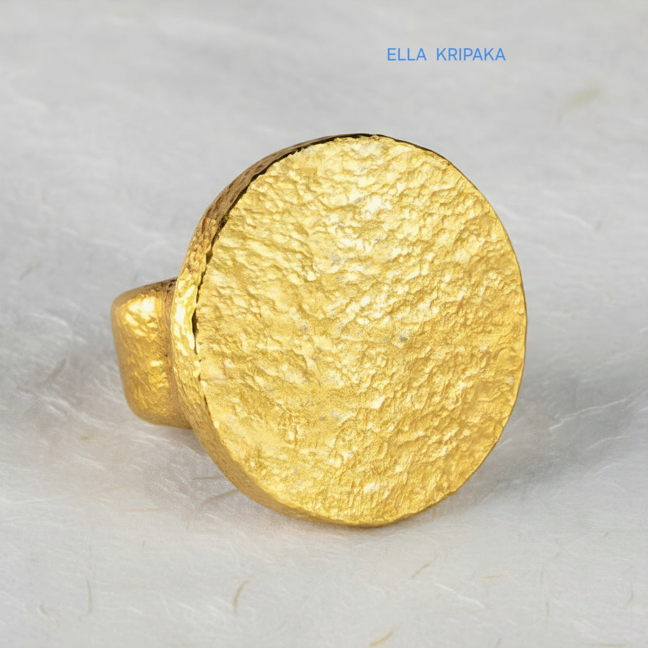 Hammered 24k 9999 Gold thick ring disk signet Ancient Rome style and Byzantine style with a textured gold on a white craft paper background, branded 'Ella Kripaka'