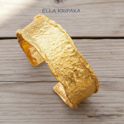 Organic hammered 24k 9999 gold bracelet uneven cuff on a old wooden background, branding artist-jeweler name 'Ella Kripaka'