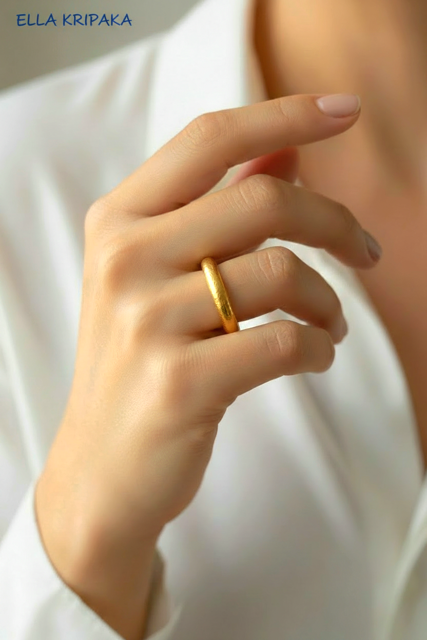 Close-up of a woman's hand wearing a 24k hammered thick gold ring with a soft focus background, with artist-jeweler 'Ella Kripaka' branding