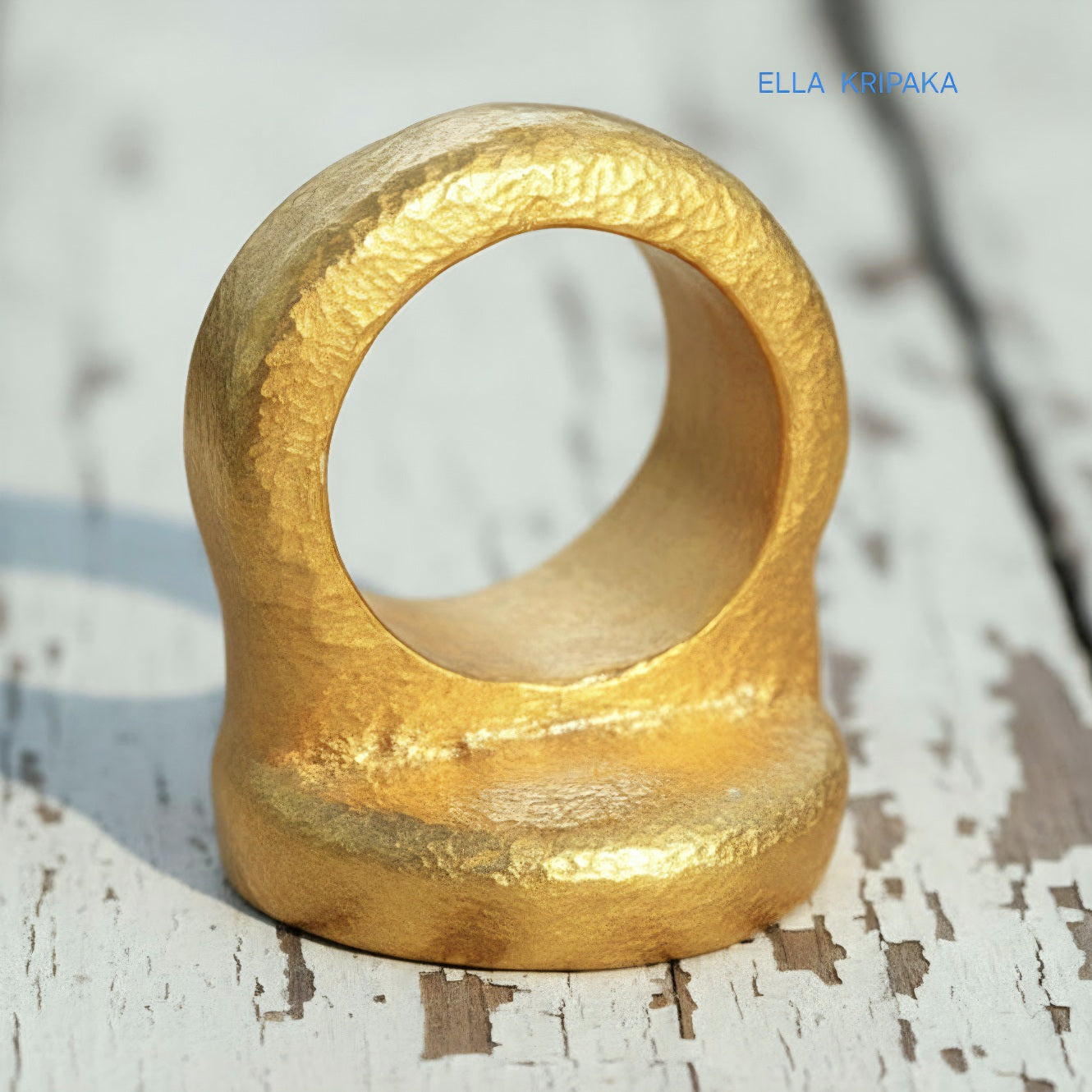 Hammered 24k 9999 Gold thick ring disk signet Ancient Rome style and Byzantine style with a textured gold on a white old wooden background, branded 'Ella Kripaka'