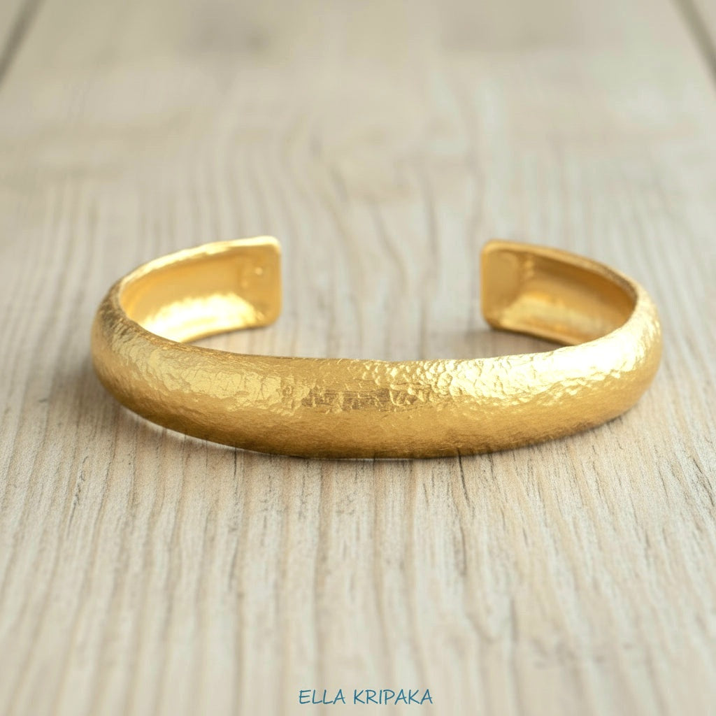 24k 9999 gold hammered Ancient Rome style bracelet cuff on old wooden background, indicating it is a custom-made jewelry with creator's name 'Ella Kripaka'
