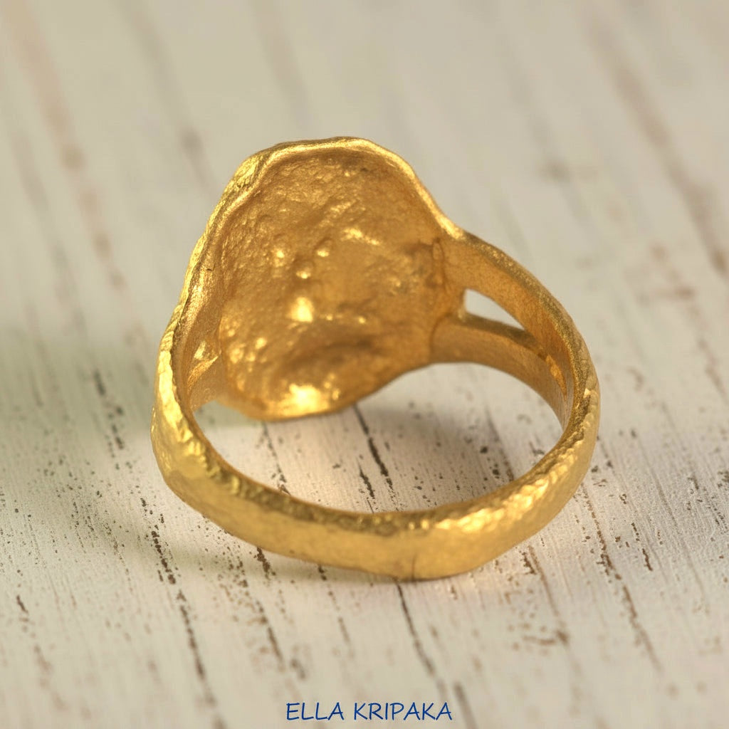 Organic 24k gold convex signet with textured uneven design on the backdide and on a light rustic wooden surface, branded 'Ella Kripaka'