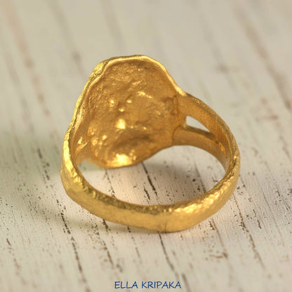 Organic 24k gold convex signet with textured uneven design on the backdide and on a light rustic wooden surface, branded 'Ella Kripaka'