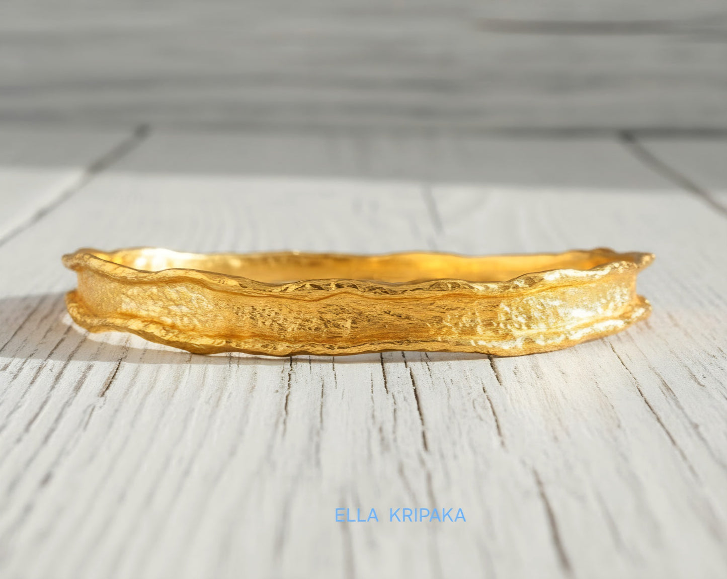 Hammered 22k gold organic textured bangle bracelet with uneven edges on old white wooden surface with 'Ella Kripaka' branding