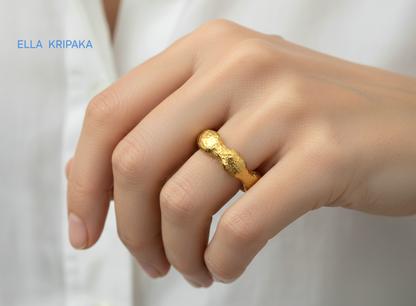 Hammered 24k 9999 Gold thick uneven wavy ring organic with a textured gold surface worn on woman's finger and on a blurred white background, branded 'Ella Kripaka'