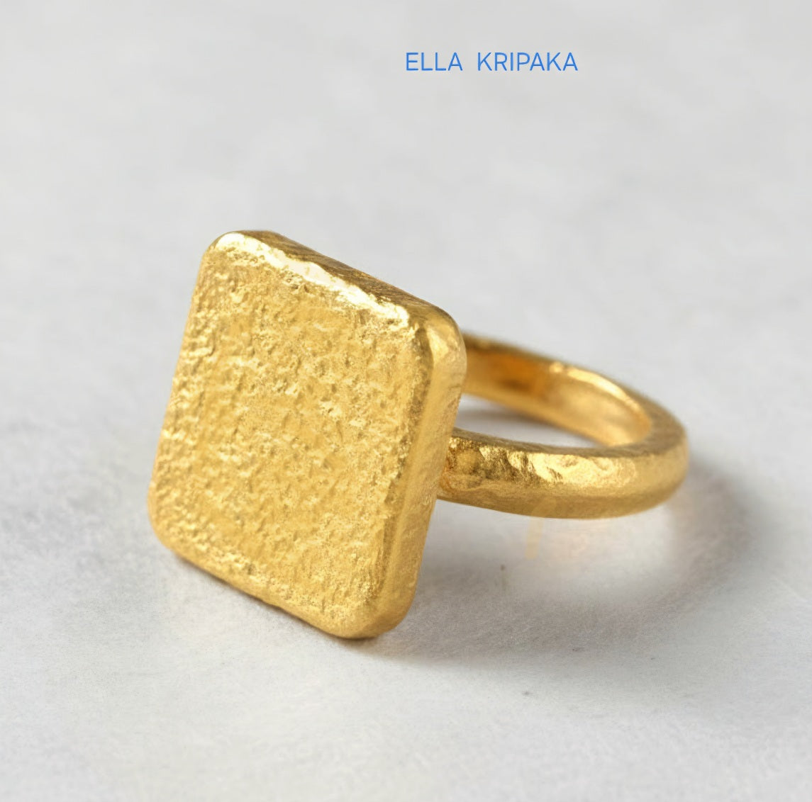 Hammered 24k 9999 Gold thick ring square signet Ancient Rome style with a textured forged gold surface on a white craft paper background, branded 'Ella Kripaka'