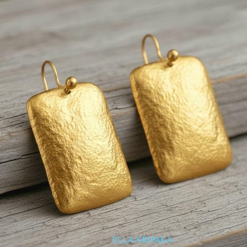 Hammered 24k gold, pure 9999 gold convex rectangular earrings with shiny forged gold textures on old wooden surface, artist-jeweler 'Ella Kripaka' branding