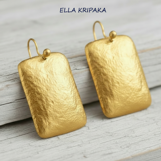 Hammered 24k gold convex rectangular earrings with shiny forged gold textures on white old wooden surface, artist-jeweler 'Ella Kripaka' branding