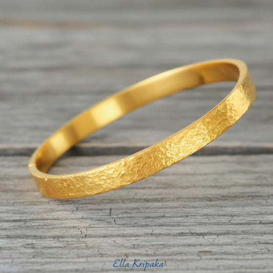 Hammered 24k 9999 gold bangle thick bracelet Ancient Rome style on an old wooden background, artist-jeweler name 'Ella Kripaka' branding