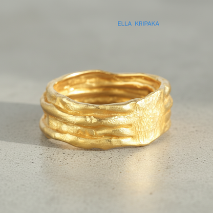 Organic hammered 24k 9999 gold convex ring with uneven thick edges on grey surface, artist-jeweler's name 'Ella Kripaka' is written in picture
