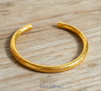 24k 9999 gold hammered Ancient Rome thick cuff bracelet on a grey old wooden surface, branded 'Ella Kripaka'