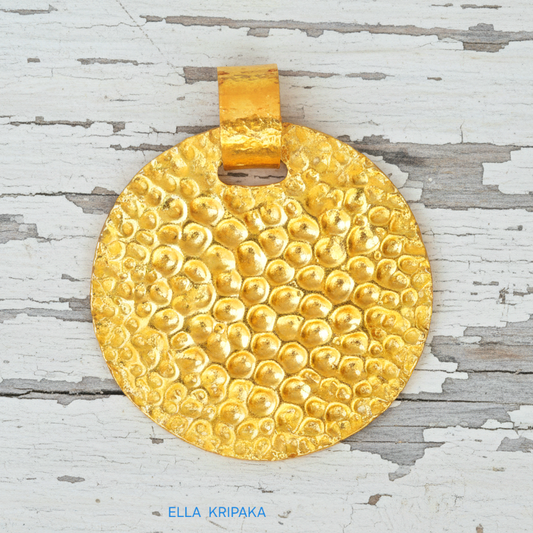 Organic hammered 24k gold, pure 9999 gold disk pendant with shiny forged gold textures on  white old wooden surface, artist-jeweler 'Ella Kripaka' branding