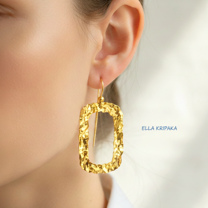 Organic hammered uneven 24k 9999 Gold hoop earrings worn by a model on a white background on a grey wooden surface, and with 'ELLA KRIPAKA' branding