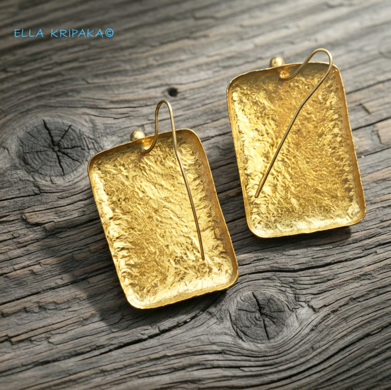Hammered 24k gold, pure 9999 gold convex rectangular earrings with shiny forged gold textures on old wooden surface, artist-jeweler 'Ella Kripaka' branding