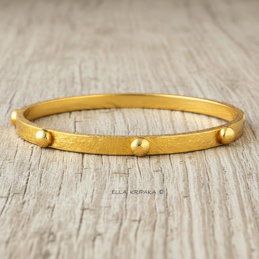 24k gold hammered bangle textured bracelet with convex rounds on light grey rustic wooden surface, artist 'Ella Kripaka' branding