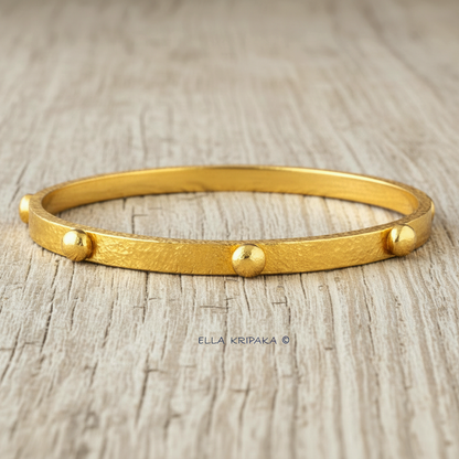 24k gold hammered bangle textured bracelet with convex rounds on light grey rustic wooden surface, artist 'Ella Kripaka' branding