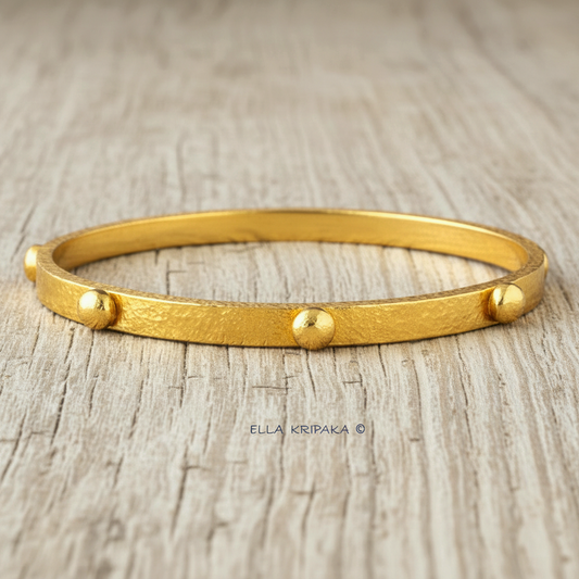 24k gold hammered bangle textured bracelet with convex rounds on light grey rustic wooden surface, artist 'Ella Kripaka' branding