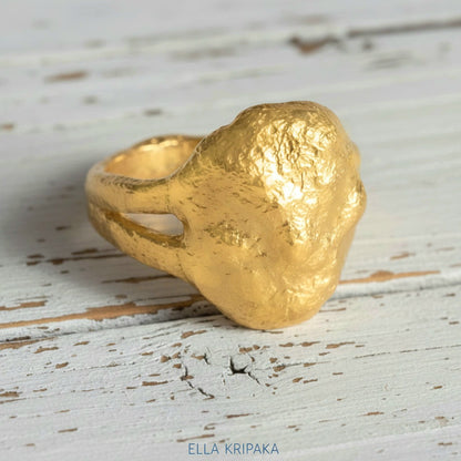 Organic 24k gold signet ring with textured uneven design on a light rustic wooden surface, branded 'Ella Kripaka'
