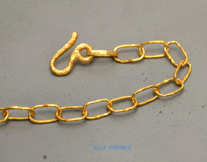 22k gold hammered chain with thick hook clasp on grey concrete background, artist-jeweler's name 'Ella Kripaka' branding