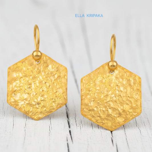 Hammered 24k gold, pure 9999 gold hexagon earrings with shiny forged gold textures on old wooden surface, artist-jeweler 'Ella Kripaka' branding