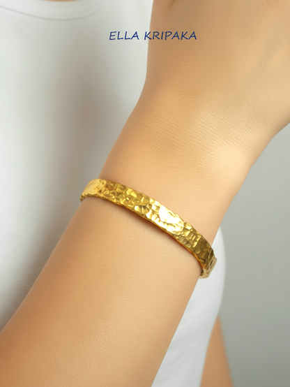 Organic hammered 24k gold bracelet cuff with uneven edges and textured design is worn by a woman on wrist and on white t-shirt background, branding artist 'Ella Kripaka'